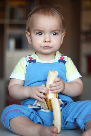 Happy funny toddler boy eating banana fruit, healthy food eating concept, indoor portraitの写真素材