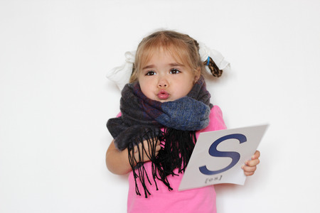 Pretty little girl in the scarf with S letter in one hand huddling up from cold, indoor isolated portrait over the white backgroundの写真素材