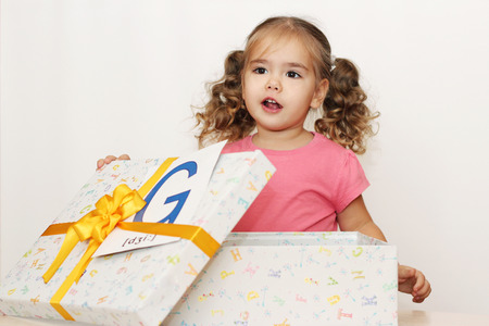 Pretty small girl with fun face opening the gift box with G letter on it, indoor portraitの写真素材
