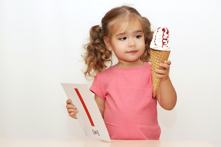 Pretty small girl eating an ice-cream on the white background with I letter on it, indoor portraitの写真素材