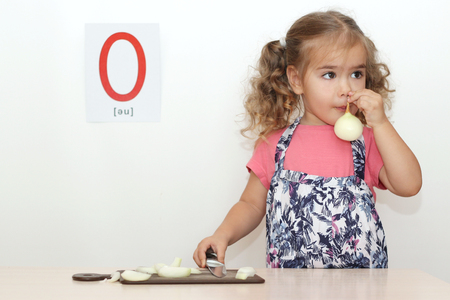 Pretty small girl smelling an onion on the white background with O letter on it, indoor portraitの写真素材