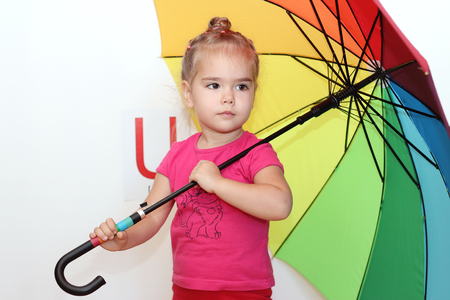Pretty small girl holding the rainbow colored umbrella on white background with U letter on it, indoor portraitの写真素材