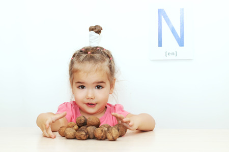 Pretty small girl scattering walnuts over white background with N letter on it, indoor portraitの写真素材