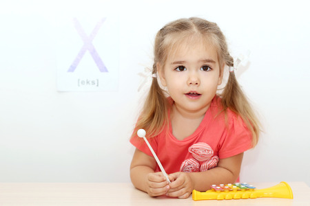 Pretty small girl playing on a xylophone over white background with X letter on it, indoor portraitの写真素材
