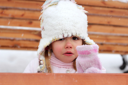 Frozen toddler girl in warm coat and knitted hat looking confused and showing her wet glove in the winter forest, outdoor portrait, winter family conceptの写真素材