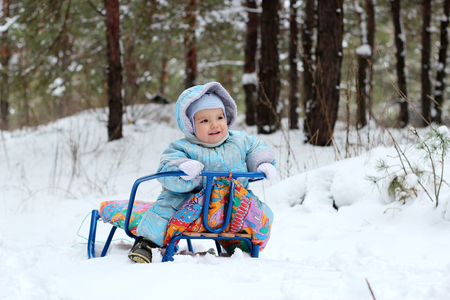 Happy little toddler boy in warm overalls sitting on the sledge in the winter forest, outdoor portrait, family spending time outdoorsの写真素材