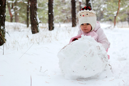 A little child girl sculpts snowman in winter landscape, winter concept, family spending time outdoorsの写真素材