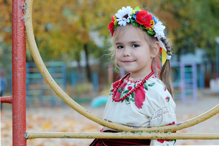 Cute Ukrainian small girl near the playground in the autumn day wearing national costume, outdoor portraitの写真素材