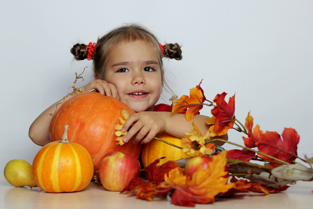 Happy small girl with pumpkins and other agriculture harvested products over white background, Thanksgiving Day and Halloween concept, indoor portraitの写真素材