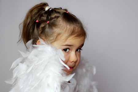 Closeup portrait of cute toddler girl in a white t-shirt with white wings as a Cupid looking over the shoulders on the white background, Saint Valentines Day card, romantic and love conceptの写真素材