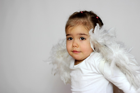 Portrait of cute toddler girl in a white t-shirt with white wings as a Cupid looking surprised and inspired over white background, Saint Valentines Day card, romantic and love conceptの写真素材