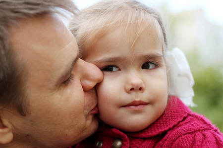 A man kissing a beautiful little girl with bows and looking on her with tenderness and love, outdoor portraitの写真素材