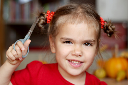 Cute little girl cutting hair to herself with scissors, funny look, indoor portraitの写真素材