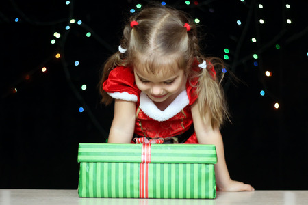 Portrait of happy little girl opening gift in the box over black Christmas background, winter holiday family conceptの写真素材