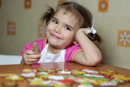Portrait of pretty little girl in white apron dreaming about a gift from Santa Claus near colorful cookies she baked and drawn for him by herself, happy family concept, winter holidayの写真素材