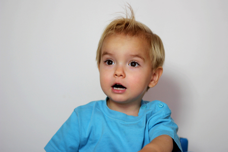 Handsome toddler boy in blue t-shirt with open mouth looking surprised over white background, child emotional portrait, indoor closeup の写真素材