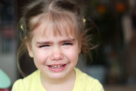 Cute preschooler blond girl crying and looking aside over dark background, emotional closeup...