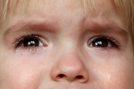 Pretty little blond boy crying and looking aside over dark background, emotional closeup portrait, upbringing and family conceptの写真素材