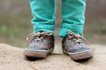 Boy in green jeans and sneakers standing on the sand in the park, close up leg's shot, beauty and...