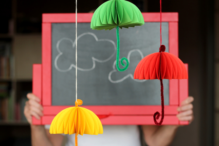 Colorful paper umbrellas hanging over blackboard with imaged clouds, place for text, selective focus, creativity and art conceptの写真素材