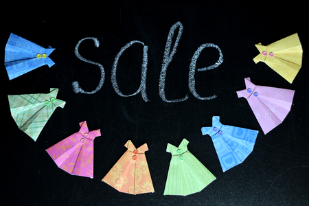 Colorful paper dresses lying on the blackboard with sale word drawn with chalk, place for text, selective focus, creativity and art concept, beauty and fashionの写真素材