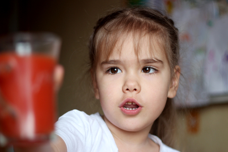 Portrait of gorgeous little girl reaching a glass of tomato juice at home, food and drink concept, healthy food, closeup indoorの写真素材