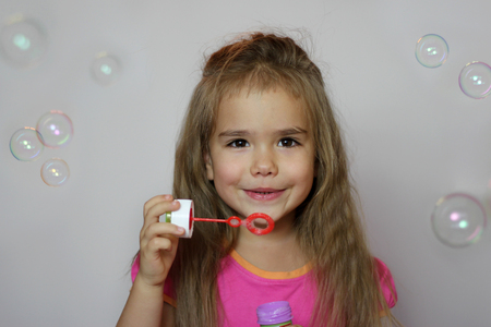 Portrait of funny little girl with long hair blowing soap bubbles over white background, happy childhood conceptの写真素材