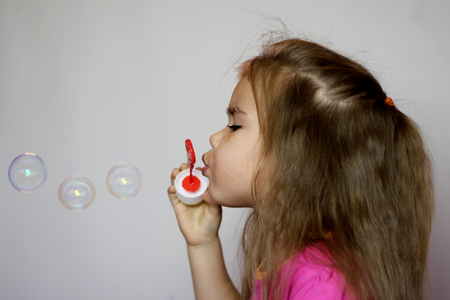 Portrait of funny little girl with long hair blowing soap bubbles over white background, happy childhood concept, sideviewの写真素材