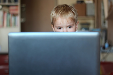Serious toddler boy works on laptop computer at home, concept for business, education, learning,...
