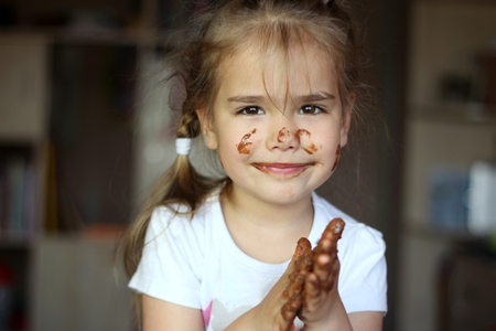 Pretty smiling girl dirty with chocolate rubbing her hands with pleasure, food and drink concept, chocolate face, indoor emotional portraitの写真素材