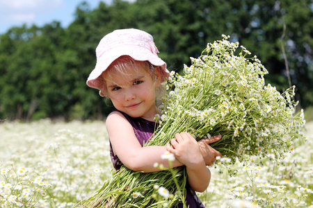 Cute little smiling girl wearing beautiful dress in the chamomile field in summer, child with huge bouquet of white flowers, beauty and fashion, happy childhood, summer vacation, closeup face outdoorの写真素材