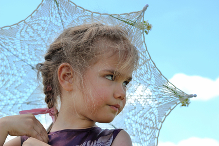 Cute little girl opens openwork sun parasol into the blue sky while she walking among the bloom chamomile field in summer, shabby chic charm, country style concept, beauty and fashion, summer outdoorの写真素材