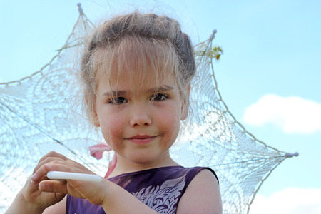 Cute little girl opens openwork sun parasol into the blue sky while she walking among the bloom chamomile field in summer, retro and country style concept, beauty and fashion, summer outdoorの写真素材