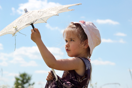 Cute little girl opens openwork sun parasol into the blue sky while she walking among the chamomile field in summer, shabby chic charm, country style concept, beauty and fashion, summer outdoorの写真素材