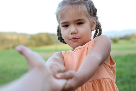 Cute happy preschool girl stretches out her arms to make go somebody for playing, summer outdoor, beautiful nature sight background, gesture and sing conceptの写真素材