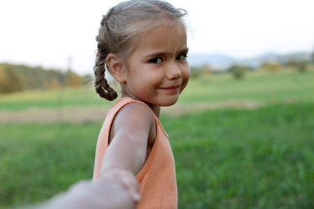 Cute happy preschool girl stretches out her arms to make go somebody for playing, summer outdoor, beautiful nature sight background, gesture and sing concept の写真素材