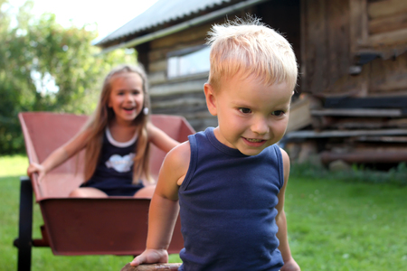 Smiling siblings, sister and brother, playing together in the backyard during their summer vacation, they riding each other in the barrow, happy childhood concept, summer outdoorの写真素材
