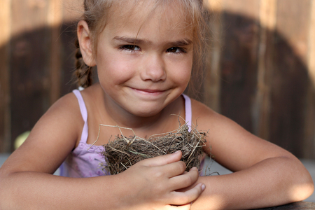 Cute preschooler girl carefully with two hands holding a real bird nest with eggs, the concept of caring, Easter, happy family and childhood, summer outdoor portraitの写真素材