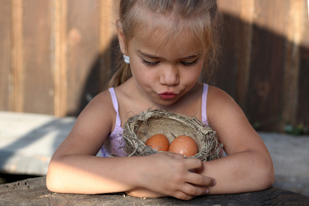 Cute preschooler girl carefully with two hands holding a real bird nest with eggs, the concept of caring, Easter, happy family and childhood, summer outdoor portraitの写真素材