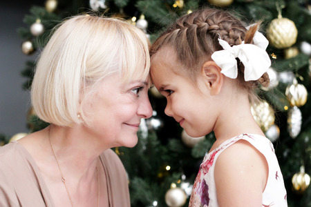 Portrait of happy grandmother and granddaughter looking to each other over Christmas present and decorated New Year tree, merry Christmas concept, happy family, lifestyle indoor, studio shotの写真素材