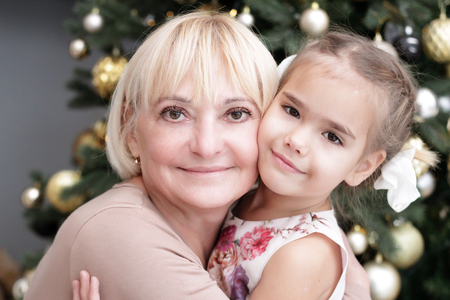 Portrait of happy granddaughter hugging her grandmother over Christmas presents and decorated New...