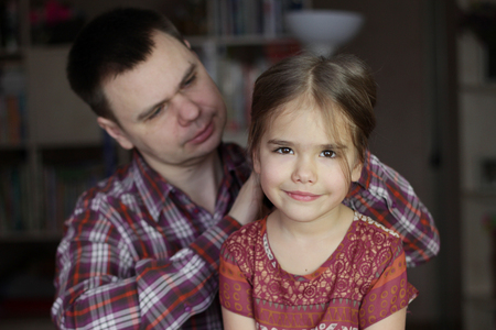 Father helps his daughter to get ready for her day by brushing her hair, father looking at his daughter with love, family relations concept, indoor lifestyleの写真素材