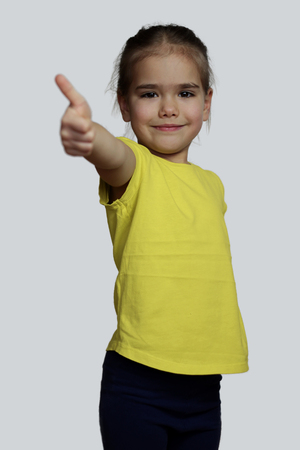 Pretty preschool girl in yellow t-shirt making the ok sign over white background, beauty and fashion conceptの写真素材