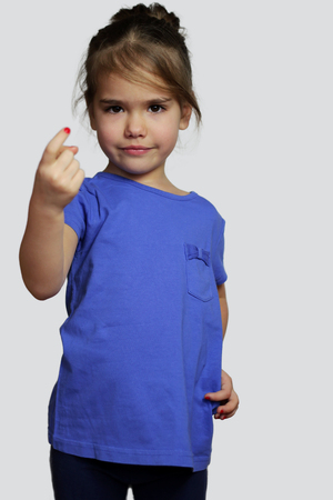 Serious pretty preschool girl in dark blue t-shirt gesturing come here calling you over white background, beauty and fashion conceptの写真素材