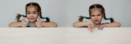 Double photo of cute 5 years old girl with funny pigtails showing like and dislike gestures with thumb up and down on white board, space for copy, advertising and announcement concept, studio shot over white backgroundの写真素材
