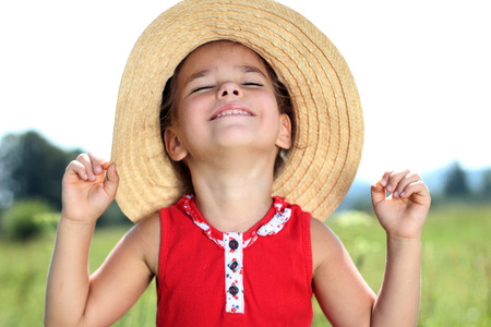 Close-up portrait of pretty happy little girl in straw hat smiling and looking at the son over meadow background, summer, vacation, travel concept, outdoor lifestyleの写真素材