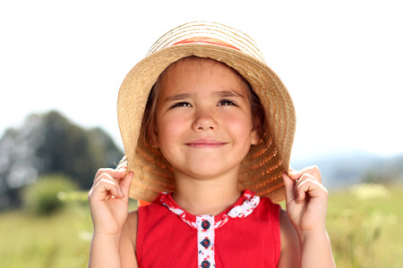 Close-up portrait of pretty happy little girl in straw hat smiling and looking at the son over meadow background, summer, vacation, travel concept, outdoor lifestyleの写真素材
