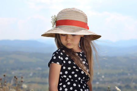 Pretty little girl in an elegant dress and straw hat relaxing on the top of the mountains, summer, vacation, travel concept, she gathers flowers, outdoor portraitの写真素材