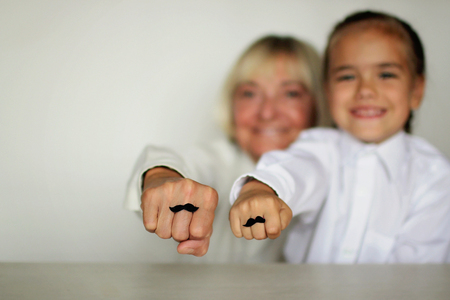 A cute little girl and her grandmother showing their fists with felt moustaches rings, happy father day and men health conceptの写真素材