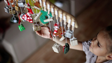 Cute little kid stretching for advent calendar with small gifts. Child searching for candy or gifts in crafted bags and boxes. Christmas decoration for children, family winter holidaysの写真素材